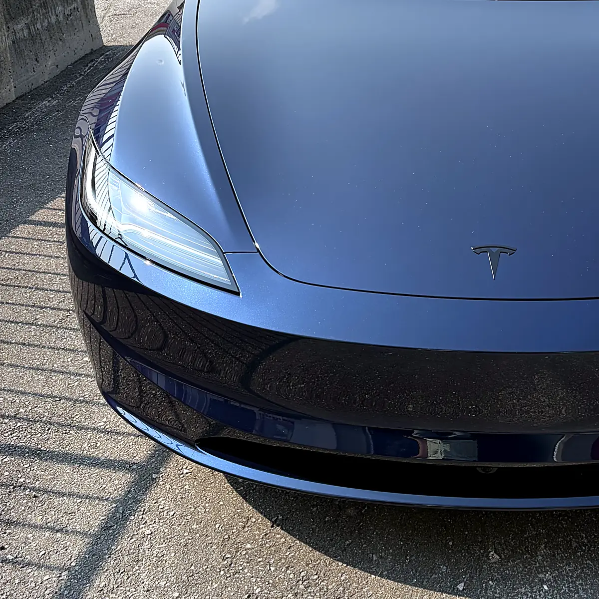 Gros plan du phare et du pare-chocs avant d’une Tesla Model 3 bleu foncé après la pose de la pellicule de protection