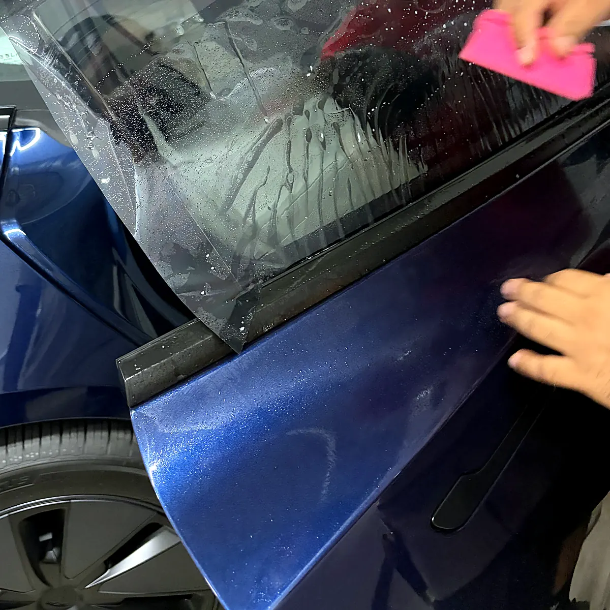 Installateur passant la raclette sur une pellicule de teinte posée sur la vitre arrière d’une Tesla Model 3, au studio Wrap Senators à Ottawa